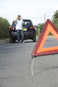 Driver Broken Down On Country Road With Hazard Warning Sign In Foreground