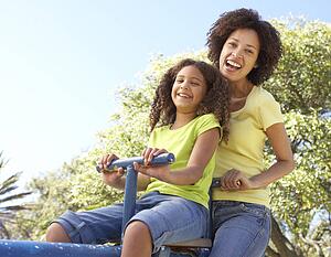 Mother And Daughter Riding On Seesaw In Park
