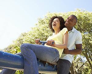 Portrait Of Young Couple Riding On SeeSaw In Park