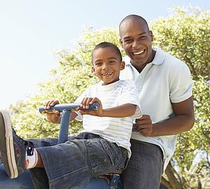 Father and Son Riding On SeeSaw In Park