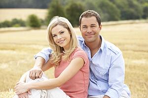 Couple Sitting On Straw Bales In Harvested Field