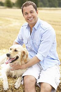 Man Sitting With Dog On Straw Bales In Harvested Field