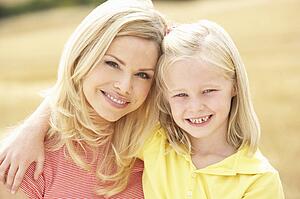 Mother And Daughter Sitting On Straw Bales In Harvested Field