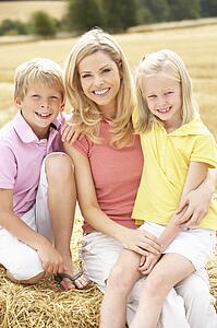 Mother And Children Sitting On Straw Bales In Harvested Field