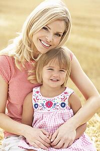 Mother And Daughter Sitting On Straw Bales In Harvested Field