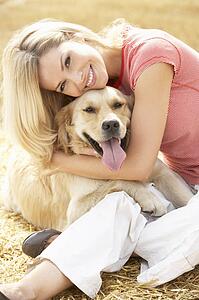 Woman Sitting With Dog On Straw Bales In Harvested Field