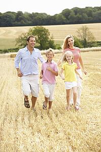 Family Running Together Through Summer Harvested Field