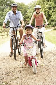 Family Cycling In Countryside Wearing Safety Helmets