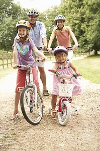 Family Cycling In Countryside Wearing Safety Helmets