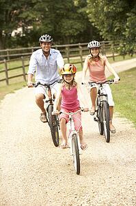 Family Cycling In Countryside Wearing Safety Helmets
