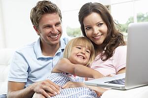 Family Sitting On Sofa Using Laptop At Home