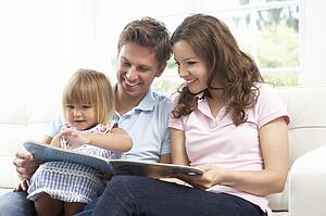 Family Sitting On Sofa Reading Book At Home