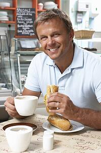 Male Customer Enjoying Sandwich And Coffee In Café 