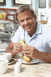 Male Customer Enjoying Sandwich And Coffee In Café 