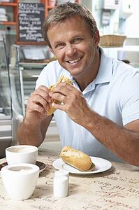 Male Customer Enjoying Sandwich And Coffee In Café 