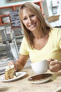 Female Customer Enjoying Slice Of Cake And Coffee In Café 