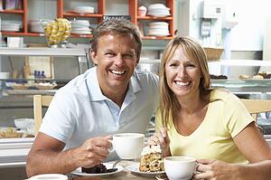 Couple Enjoying Slice Of Cake And Coffee In Café 