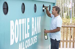 Man At Recycling Centre Disposing Of Glass At Bottle Bank