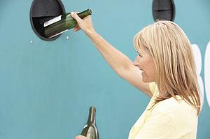 Woman At Recycling Centre Disposing Of Glass At Bottle Bank