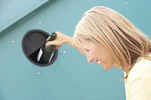 Woman At Recycling Centre Disposing Of Glass At Bottle Bank
