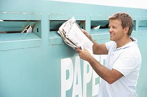 Man At Recycling Centre Disposing Of Old Newspapers