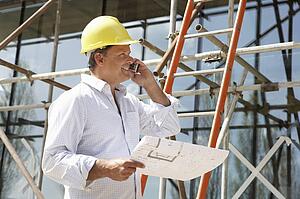 Architect With Plans Outside New Home Talking On Mobile Phone