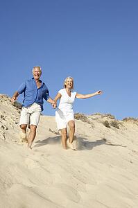 Senior Couple Enjoying Beach Holiday Running Down Dune