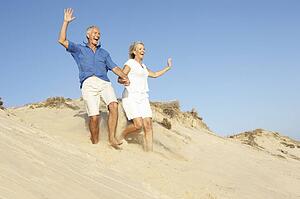Senior Couple Enjoying Beach Holiday Running Down Dune