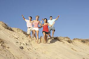 Group Of Friends Enjoying Beach Holiday Running Down Dunes