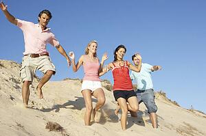 Group Of Friends Enjoying Beach Holiday Running Down Dunes