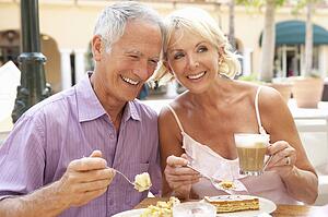 Senior Couple Enjoying Coffee And Cake In Café