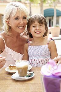 Grandmother With Granddaughter Enjoying Coffee And Cake In Café