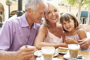 Grandparents With Granddaughter Enjoying Coffee And Cake In Café