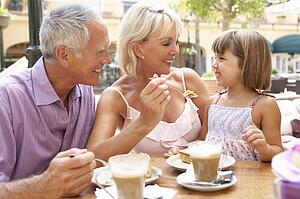 Grandparents With Granddaughter Enjoying Coffee And Cake In Café