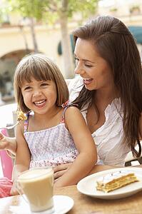 Mother And Daughter Enjoying Cup Of Coffee And Piece Of Cake In Café