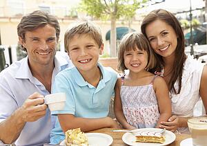 Young Family Enjoying Cup Of Coffee And Cake In Café Together