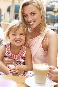 Mother And Daughter Enjoying Cup Of Coffee And Piece Of Cake In Café