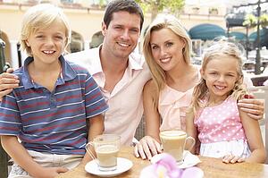 Young Family Enjoying Cup Of Coffee In Café Together