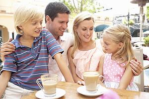 Young Family Enjoying Cup Of Coffee In Café Together