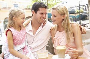 Young Family Enjoying Cup Of Coffee In Café Together