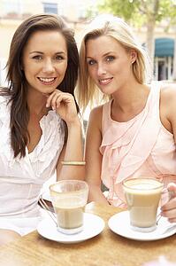 Two Young Women Enjoying Cup Of Coffee In Café