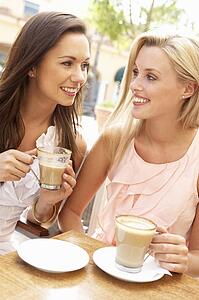 Two Young Women Enjoying Cup Of Coffee In Café