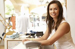 Female Sales Assistant At Checkout Of Clothing Store