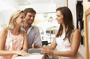 Female Sales Assistant At Checkout Of Clothing Store With Customers