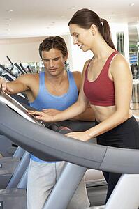 Woman Working With Personal Trainer On Running Machine In Gym