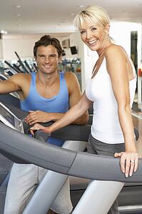 Senior Woman Working With Personal Trainer On Running Machine In Gym
