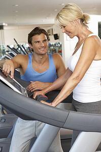 Senior Woman Working With Personal Trainer On Running Machine In Gym
