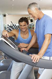 Man Working With Personal Trainer On Running Machine In Gym