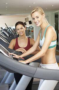 Woman Working With Female Personal Trainer On Running Machine In Gym
