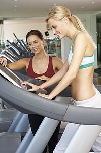 Woman Working With Female Personal Trainer On Running Machine In Gym